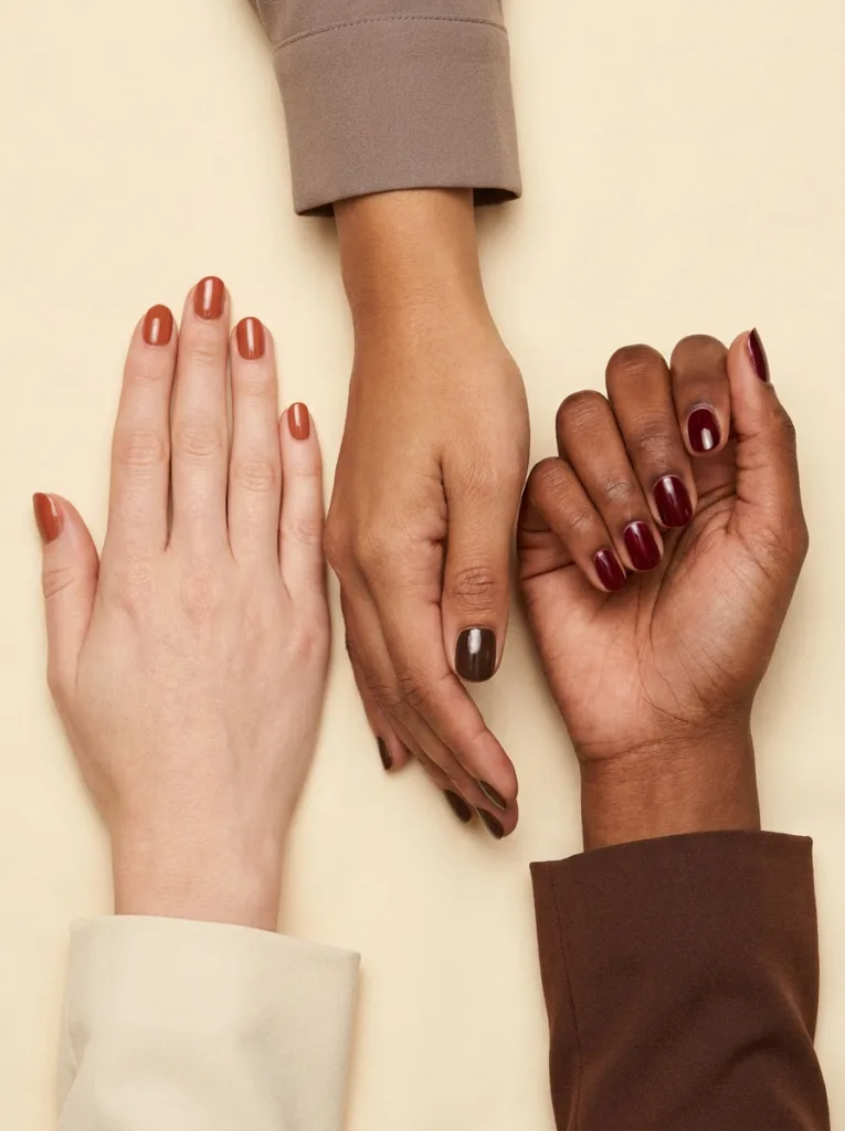 Three hands with fair, medium, and deep skin tones showing matching Thanksgiving nail colors