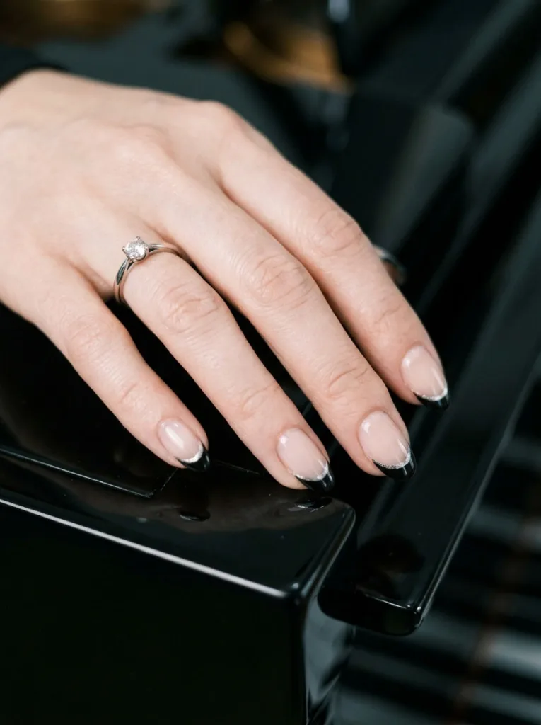 Double French tip black and silver Christmas nails resting on a piano