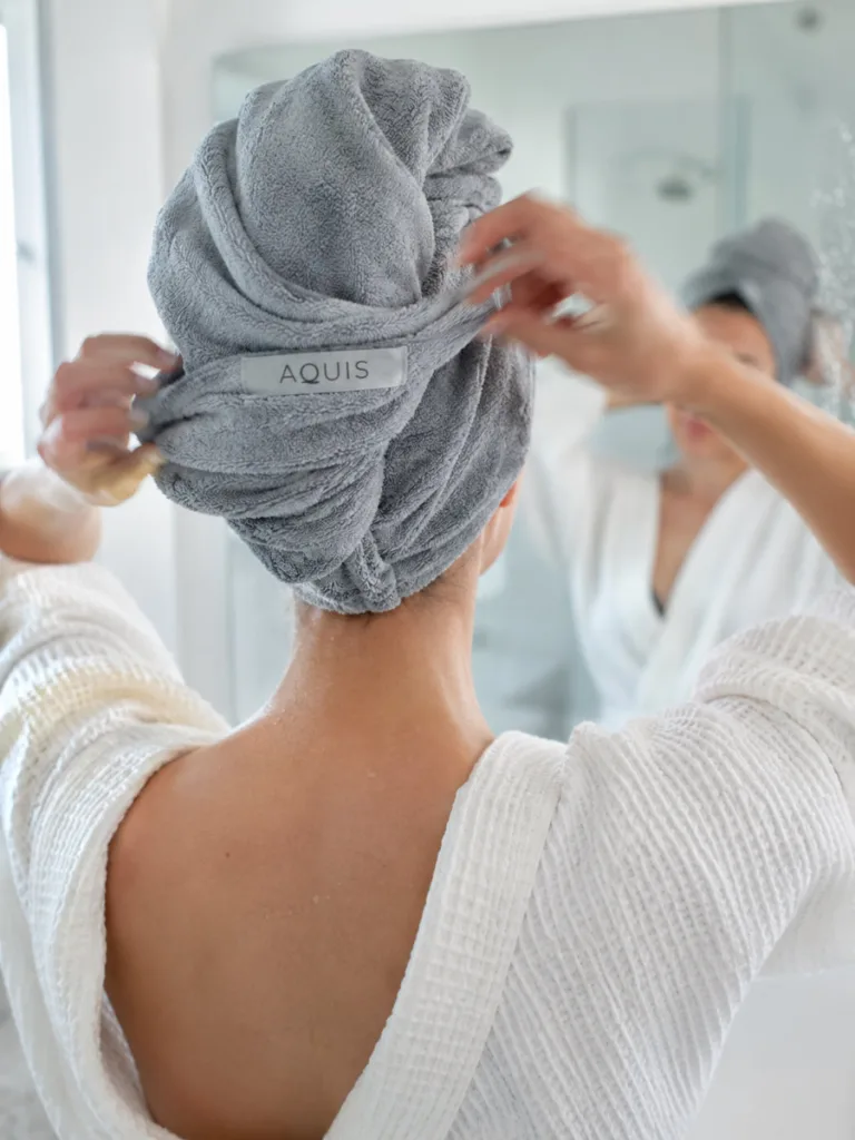 Woman wrapping her wet hair in an Aquis microfiber towel in front of a bathroom mirror