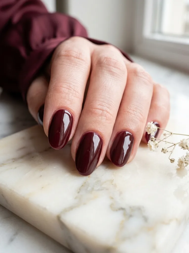 Burgundy glazed nails with ceramic high-gloss top coat showing a window reflection in each nail beside dried baby's breath on cream marble
