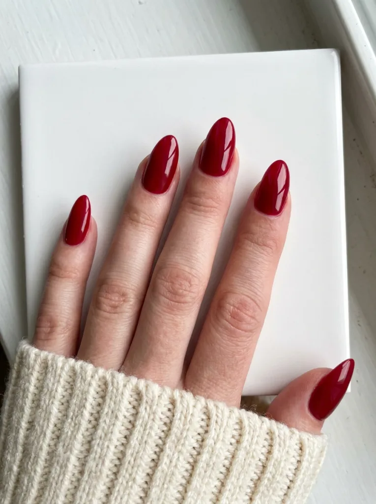 Classic cherry red almond nails with high-gloss finish on a white ceramic surface in natural window light