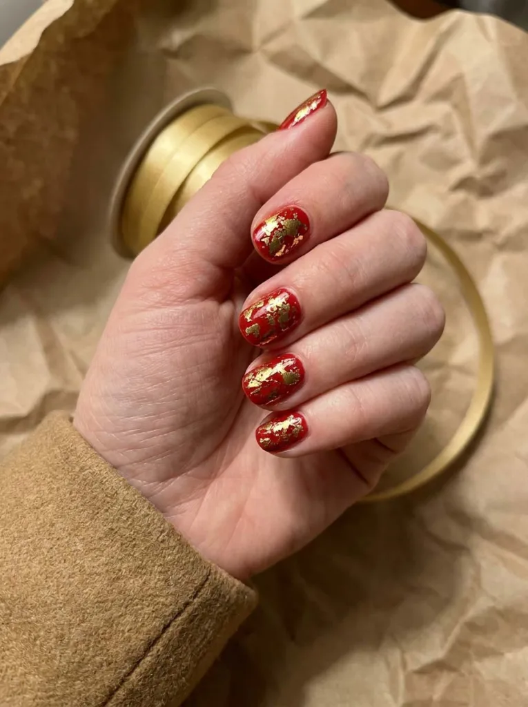 Foil-accented red christmas nails on a hand holding gold ribbon over wrapping paper