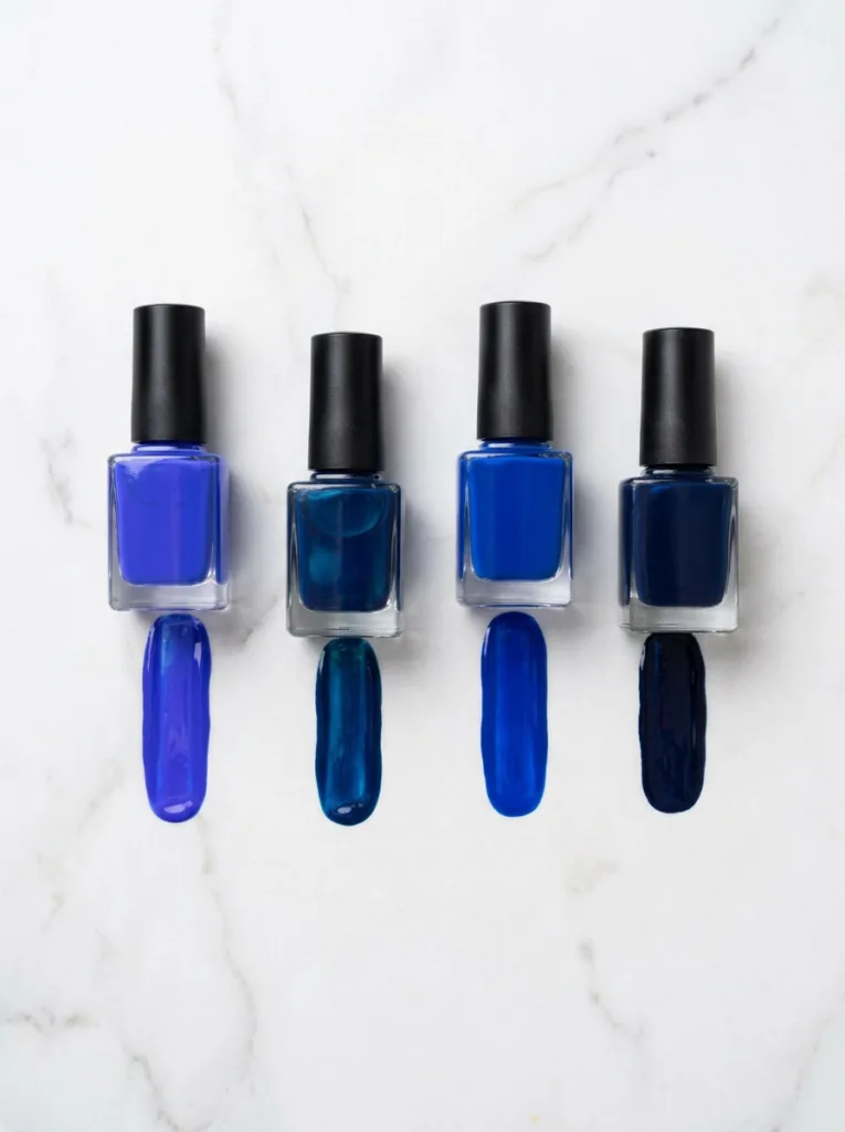 Four royal blue nail polish bottles in cobalt, sapphire, classic, and indigo shades on marble