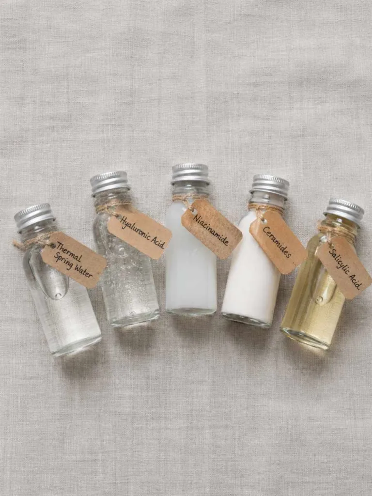 Flat lay of five glass vials representing thermal spring water, hyaluronic acid, niacinamide, ceramides, and salicylic acid