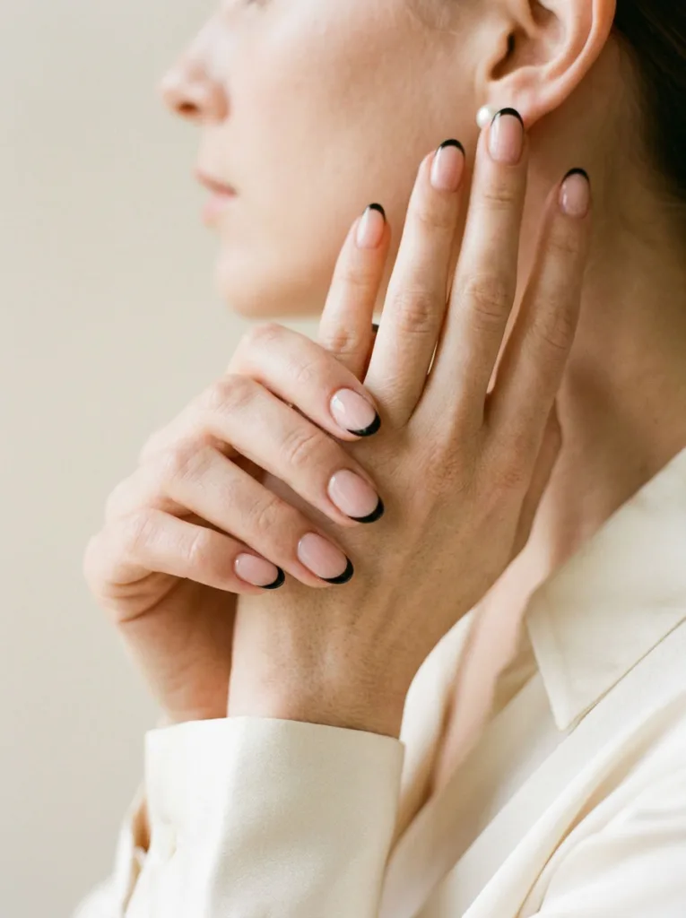 Close-up of glossy black French tip Christmas nails beside a pearl earring