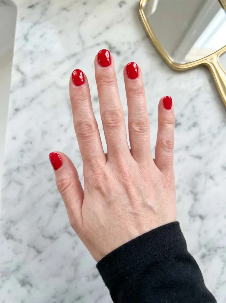 Glossy solid red christmas nails on a fair-skin hand resting on a marble vanity