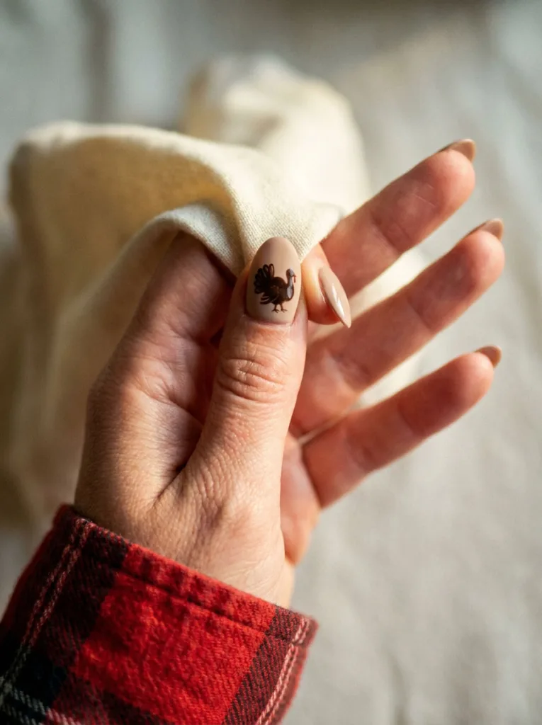 Close-up of a hand-painted turkey accent nail among neutral Thanksgiving nails