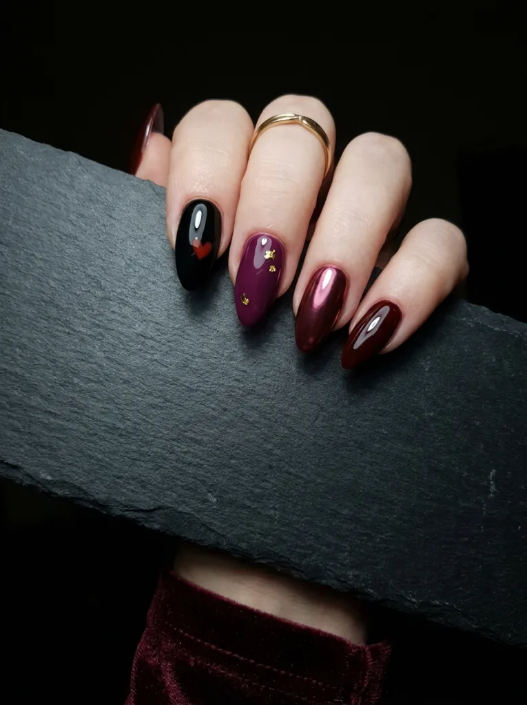 Dark valentines day nail designs on almond nails including oxblood solid, black with red heart, plum with gold foil, dark cherry chrome, and burgundy glazed