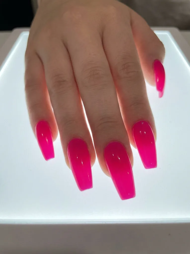 Hot pink coffin nails in saturated fuchsia on a backlit frosted glass surface showing the full vivid color