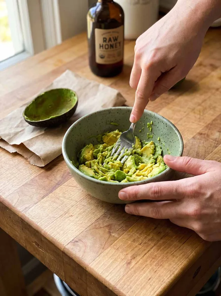 mashing ripe avocado with fork in small ceramic bowl to make homemade winter skin face mask