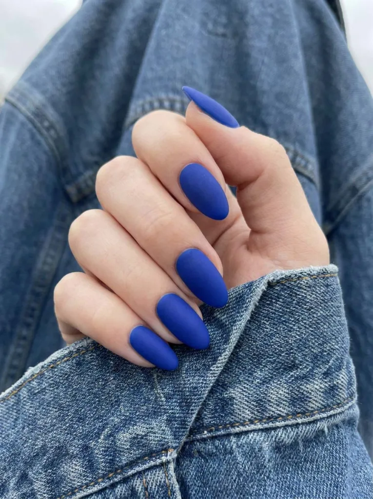 hand with matte royal blue nails resting on a denim jacket