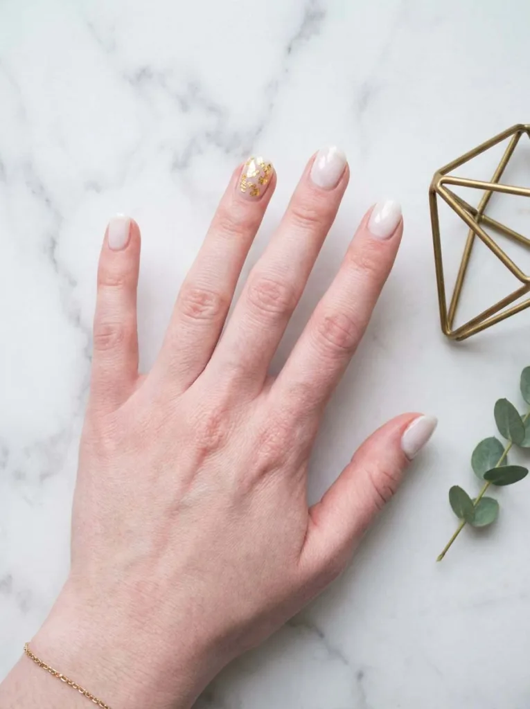 Milky white winter nails with gold leaf accent nail on marble surface
