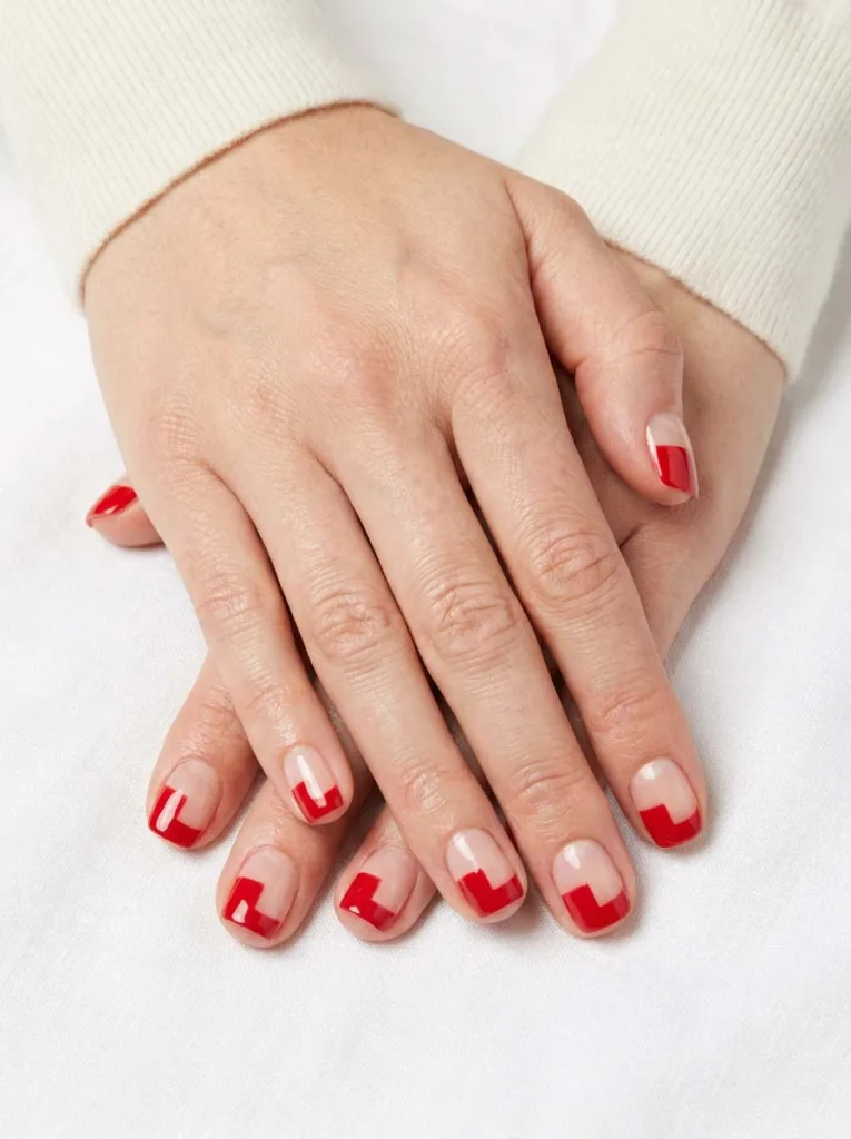 Negative space red christmas nail design on a fair-skin hand against white linen