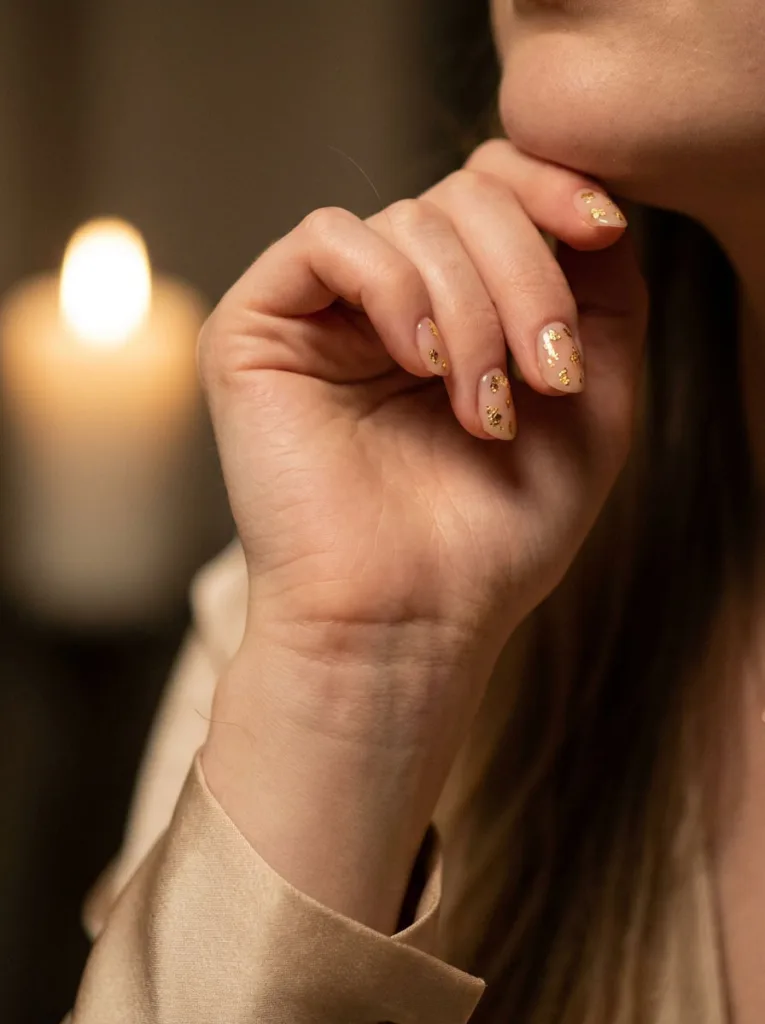 Close-up of sheer nude nails with scattered gold fleck detailing