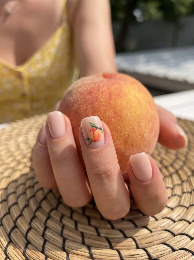 Peach fruit nail art accent nail next to a real peach