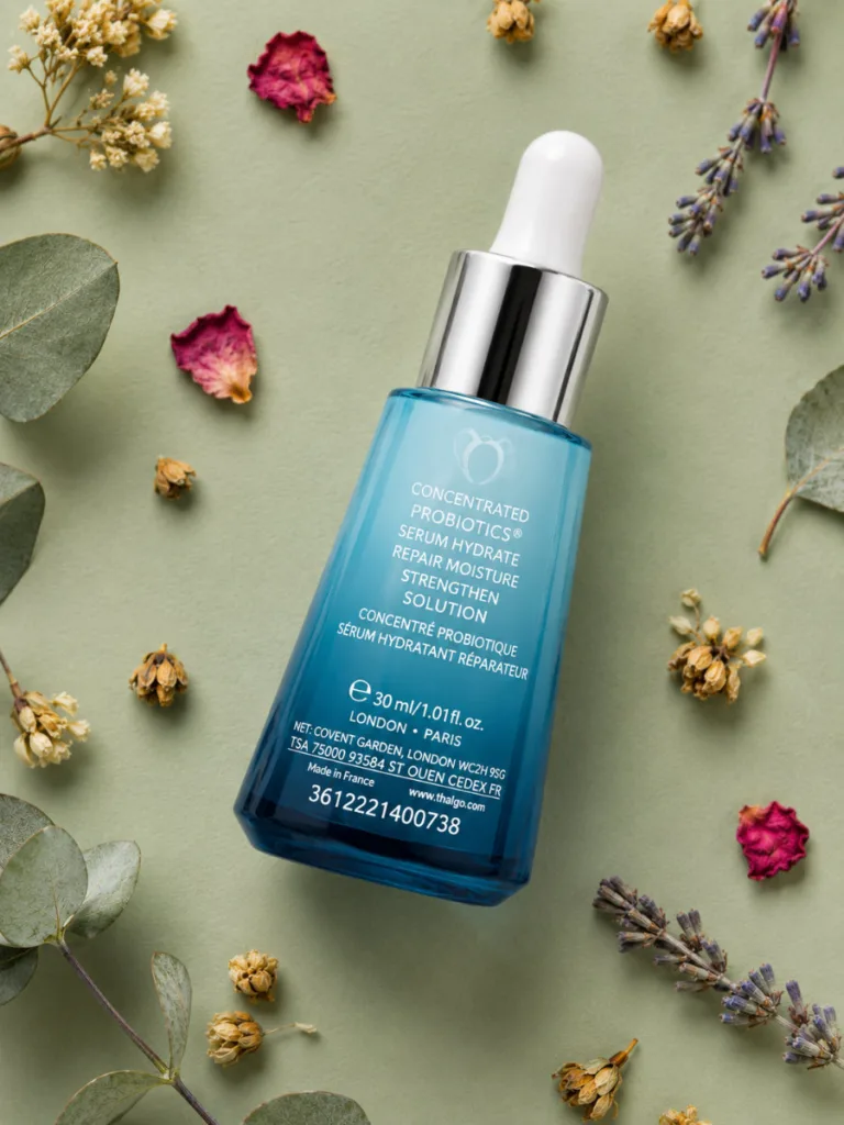 Probiotic skincare serum bottle styled in a flat-lay on a green background