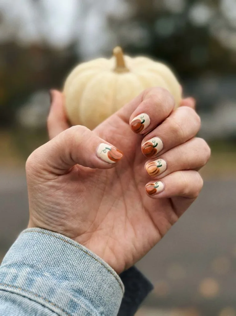 Close-up of pumpkin patch nail art on a cream and orange base