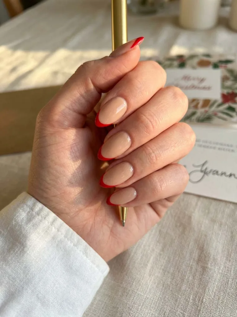 Red french tip christmas nails on a hand writing a holiday card