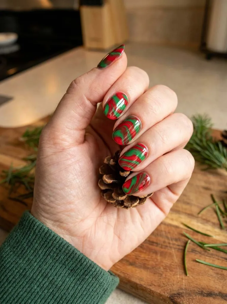 Red and green swirl christmas nails on a hand holding a pinecone