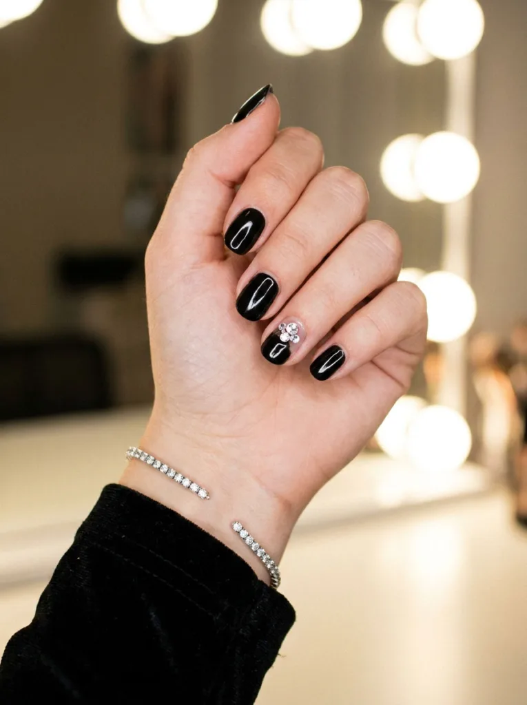 Rhinestone cluster black Christmas nails beside a diamond bracelet