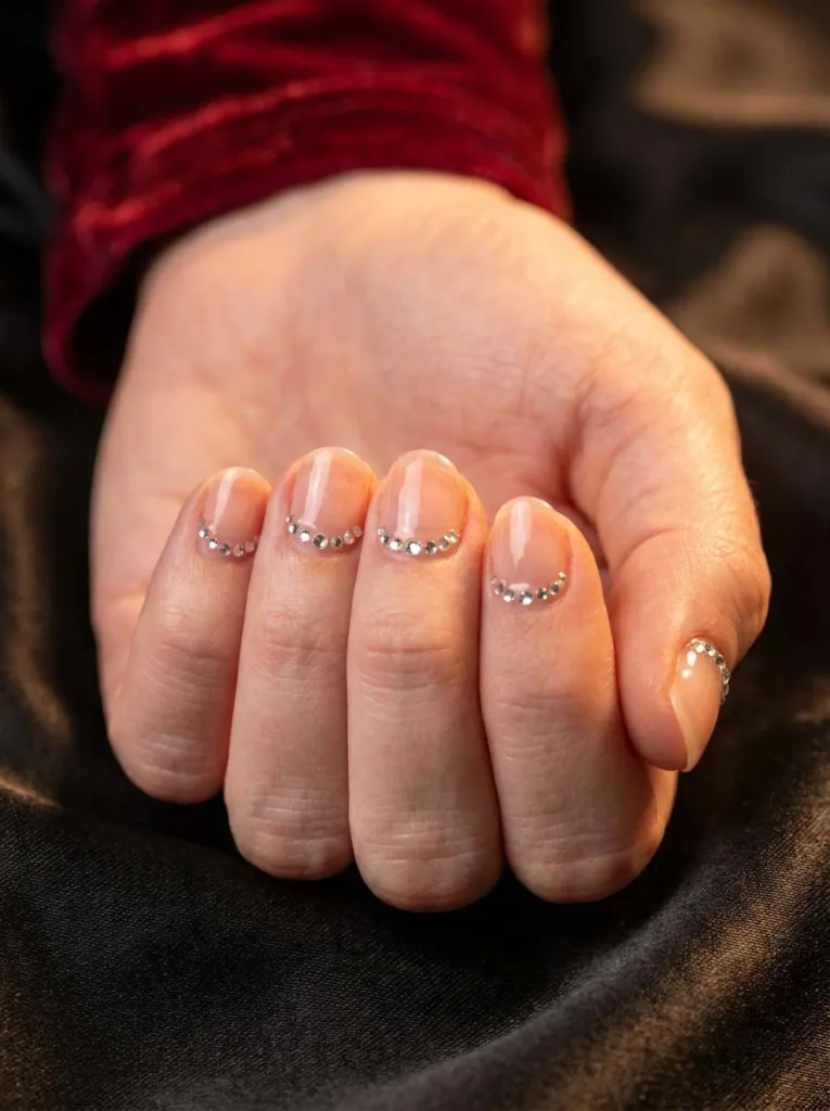 Red christmas nails with a rhinestone cuticle line on dark satin fabric