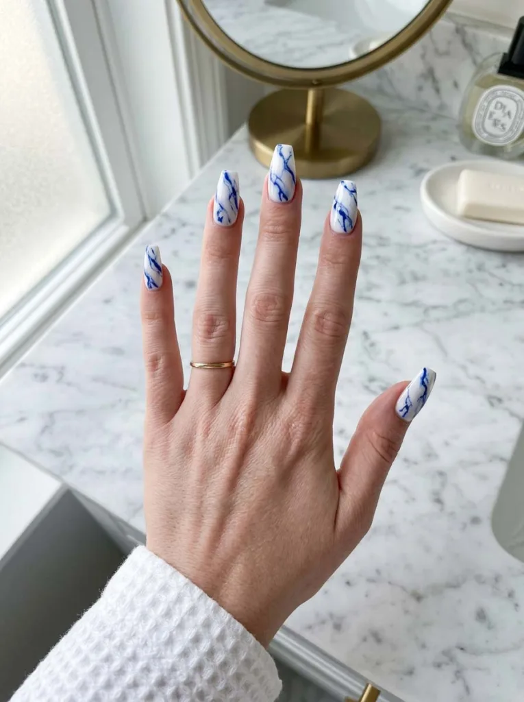 hand with a royal blue evil-eye accent nail holding sunglasses outdoors
