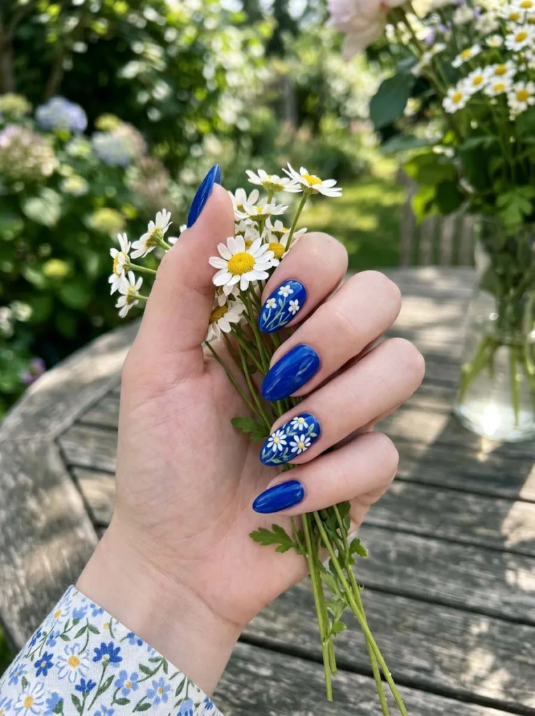 hand with royal blue floral nail art holding white daisies outdoors