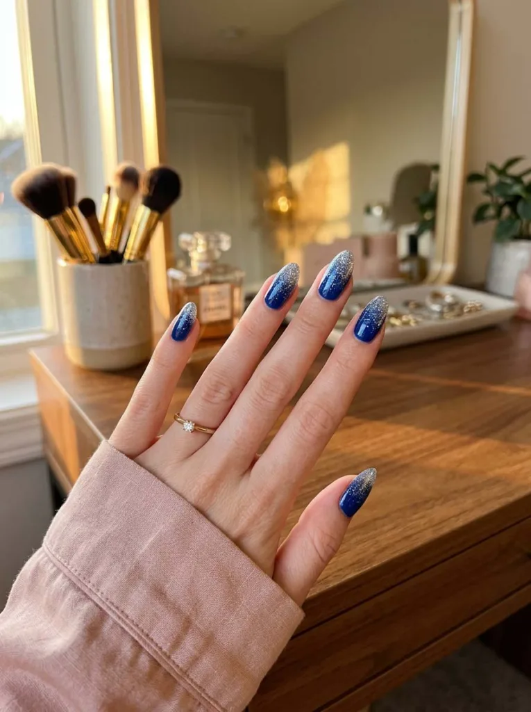 hand with royal blue glitter ombre nails resting on a vanity table