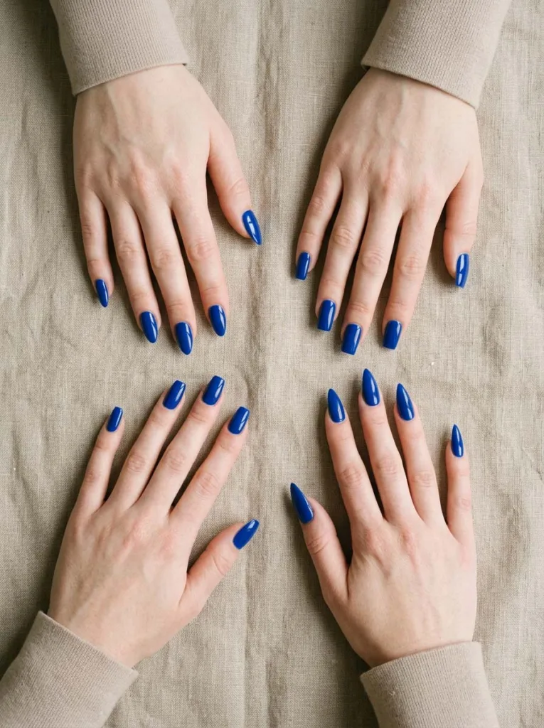 Four fair-skinned hands showing almond, coffin, square, and stiletto royal blue nail shapes