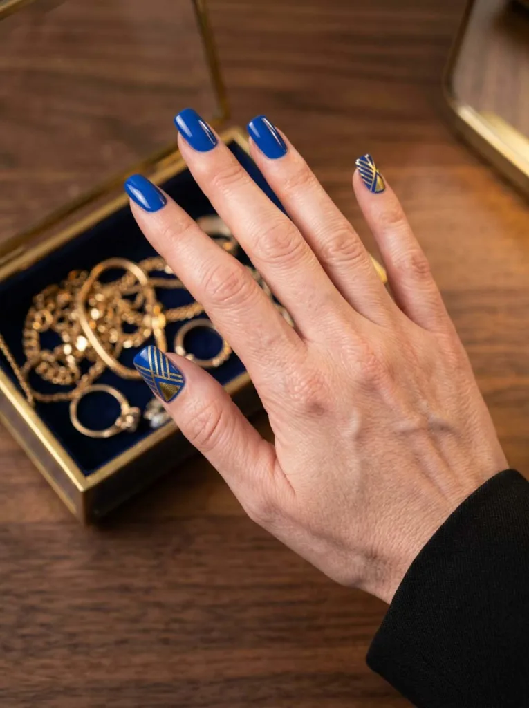 hand with royal blue and gold geometric nail art near a jewelry box