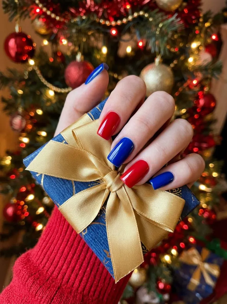 Fair-skinned hand with royal blue and red holiday nails holding a wrapped gift