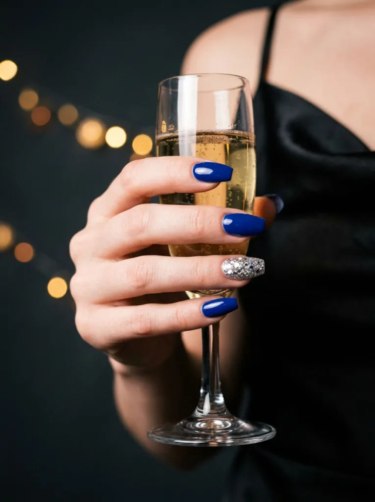 hand with silver glitter accent royal blue nails holding a champagne glass