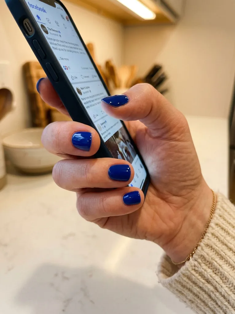 hand with short round royal blue nails holding a smartphone
