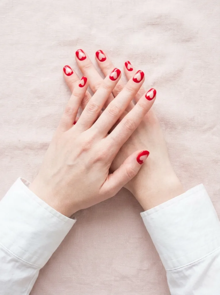 Negative space red heart nails where the bare nail forms the heart shape surrounded by red polish on both hands interlaced