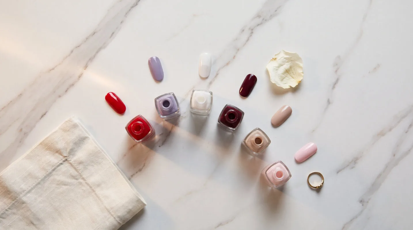 Six attractive nail color ideas as painted nail swatches and polish bottles on white marble with dried petals