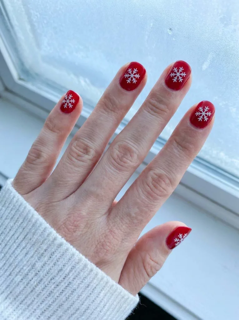 Red christmas nails with a white snowflake accent against a frosted window