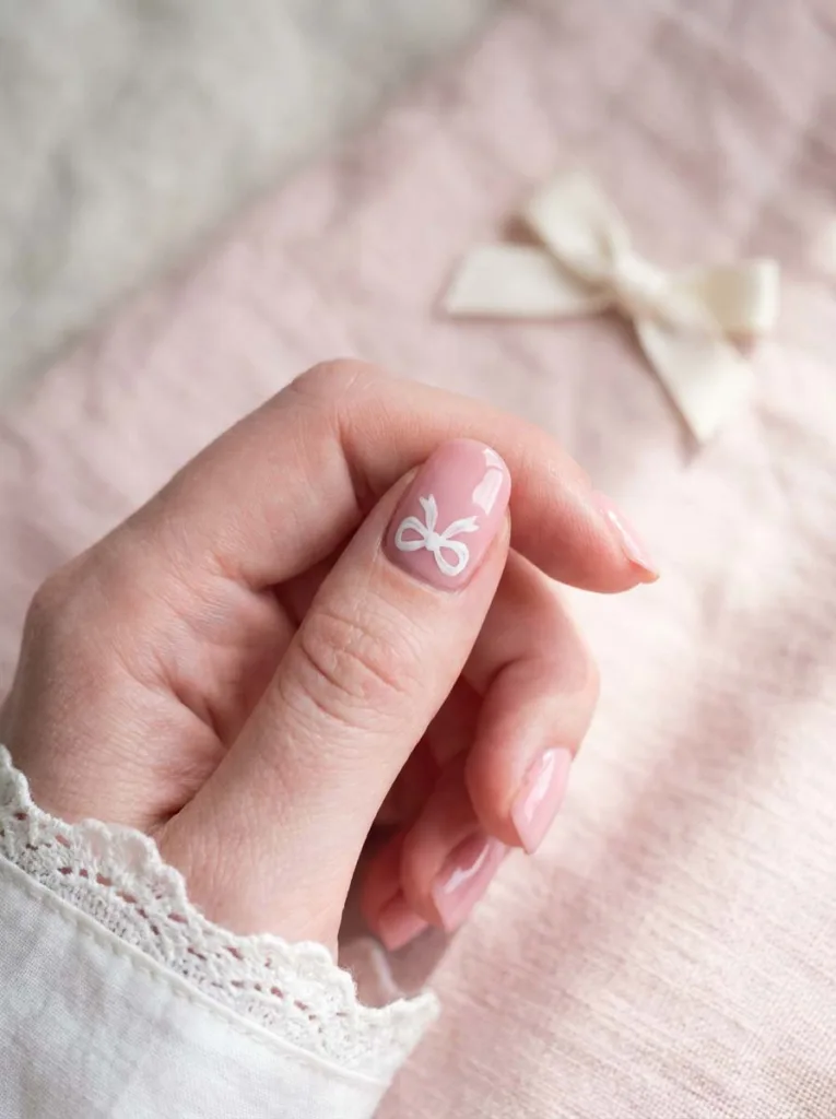 Soft pink winter nails with hand-painted bow design on ring finger