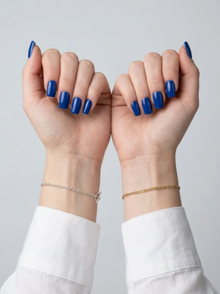 Two fair-skinned wrists with silver and gold jewelry comparing royal blue nail undertones