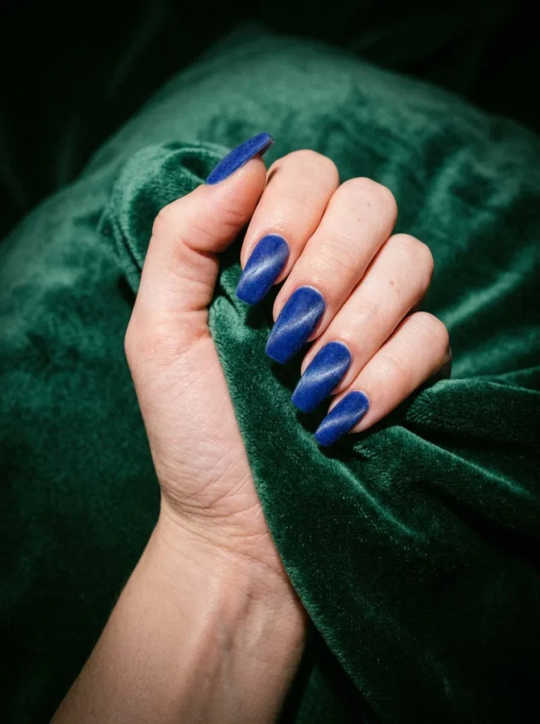 hand with velvet cat-eye royal blue nails resting on green velvet fabric