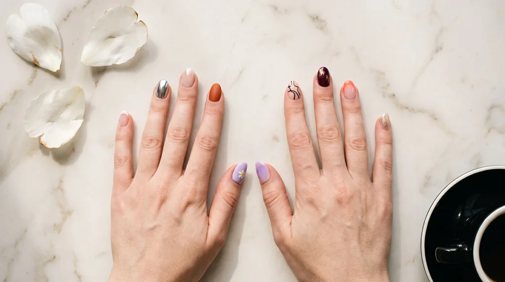 Best nail designs ideas for 2026 — a flat-lay showing French tips, chrome, glazed donut, burnt orange matte, and aura gradient nails on white marble