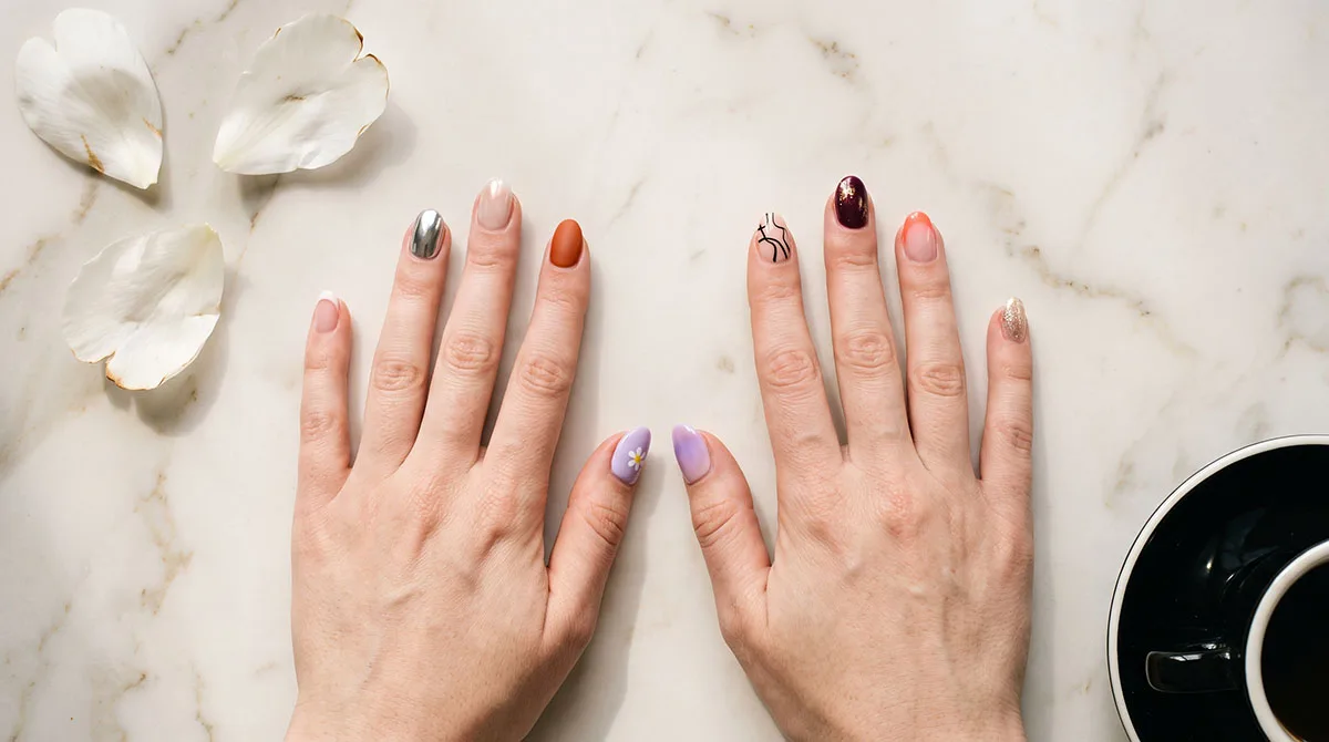 Best nail designs ideas for 2026 — a flat-lay showing French tips, chrome, glazed donut, burnt orange matte, and aura gradient nails on white marble