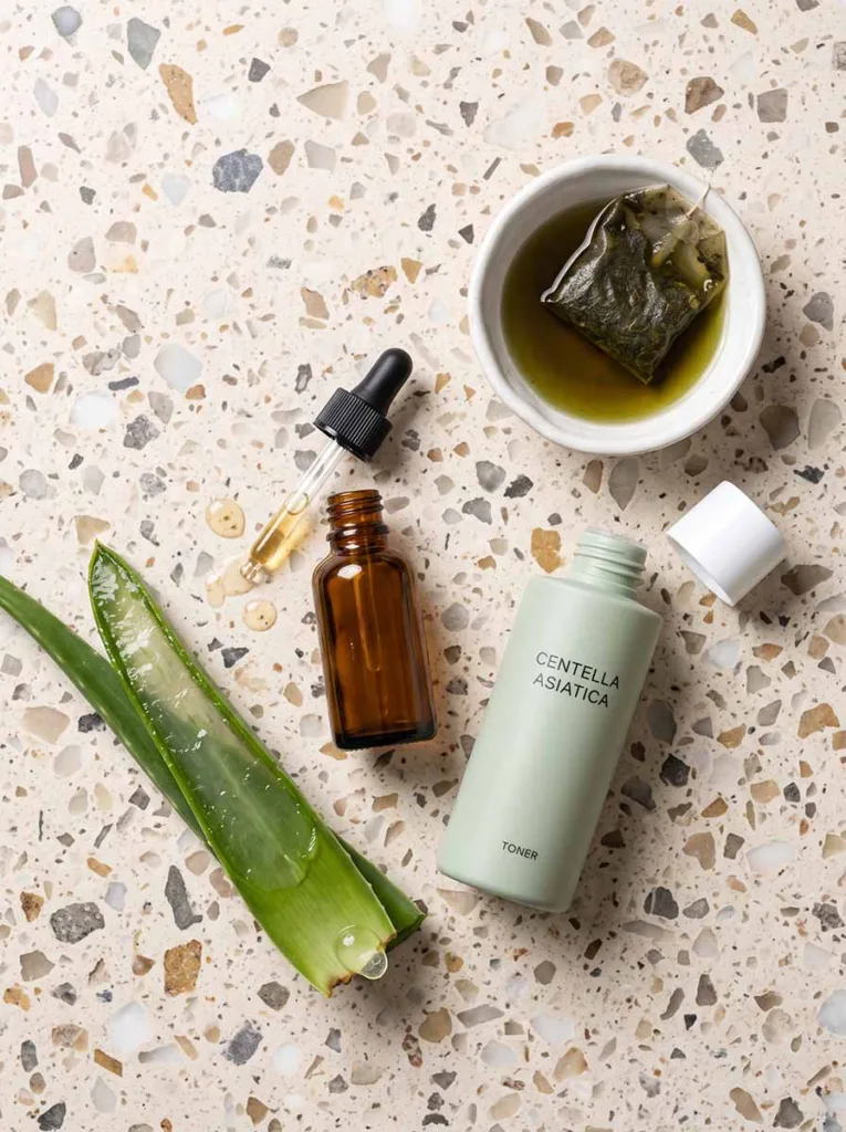 niacinamide serum, centella asiatica toner, fresh aloe vera leaf, and green tea on terrazzo surface