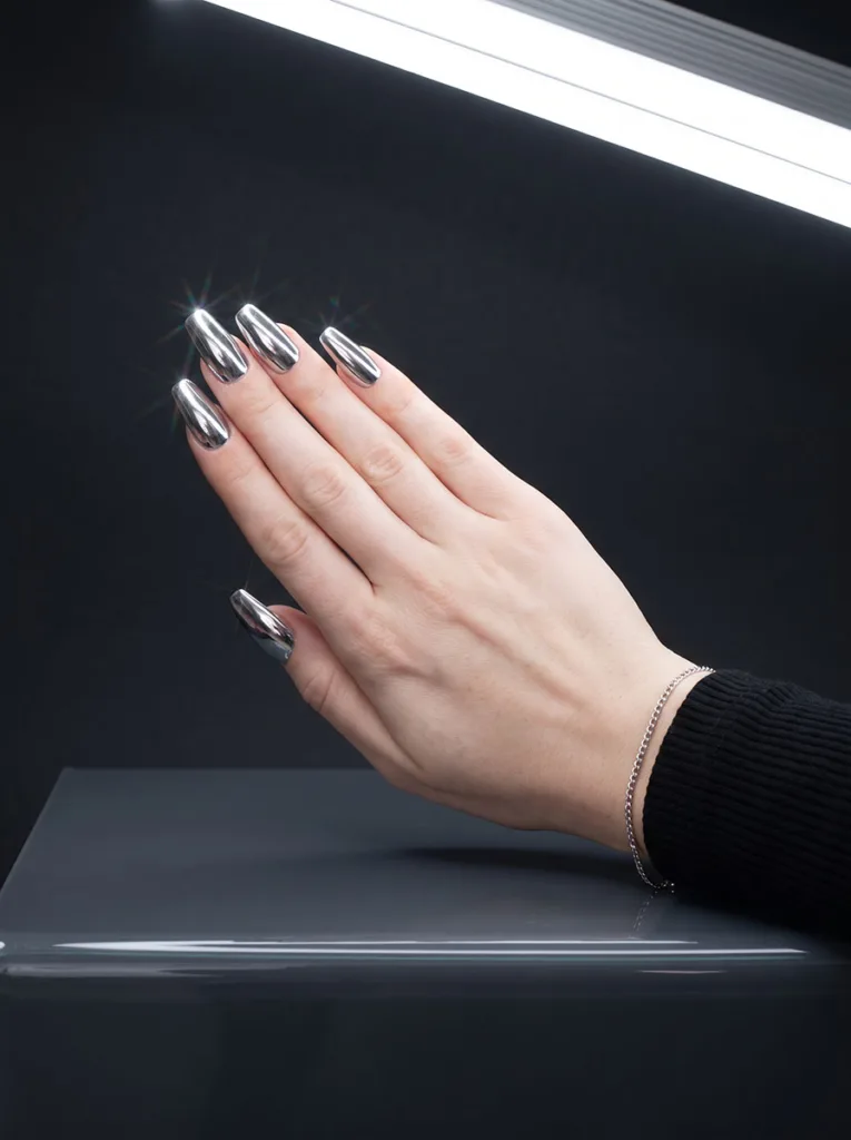 Silver chrome mirror finish nails on coffin-shaped fair-skinned hand angled toward camera on dark grey studio background
