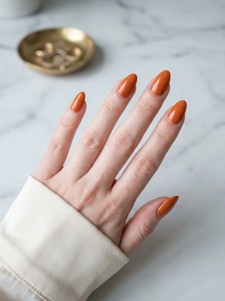 Hand with classic glossy orange nail polish resting on a marble table