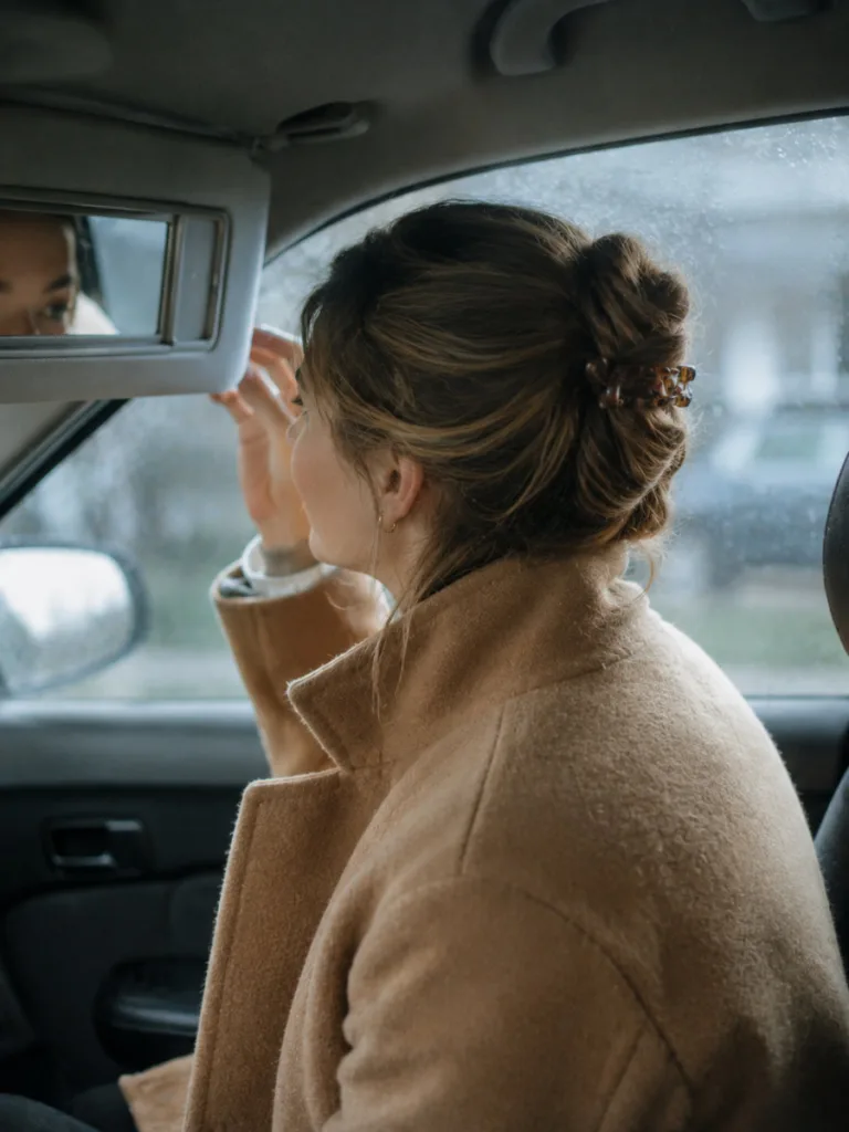 Woman checking a dressy French twist Thanksgiving hairstyle in a car mirror