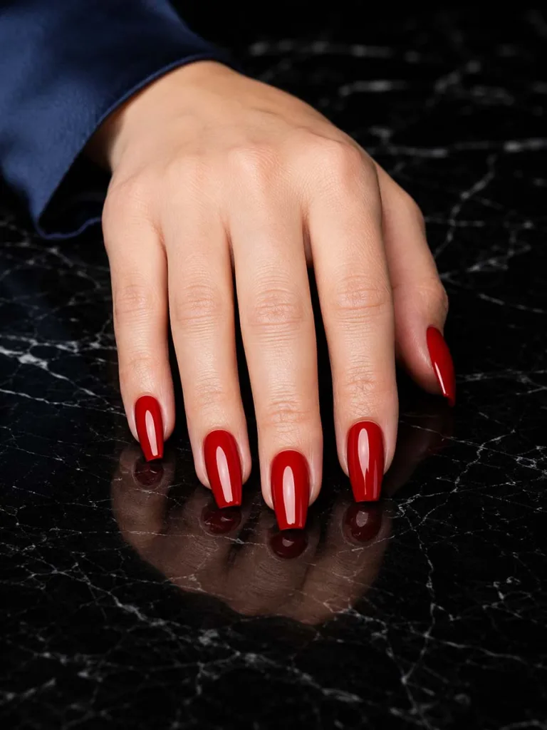 Glossy cherry red coffin nails pressed flat on black marble surface with reflection, shot straight-on under studio lighting