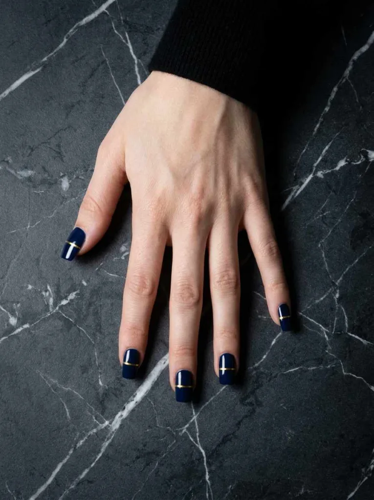 single gold horizontal stripe nail art on deep navy base square nails fair skin overhead dark marble