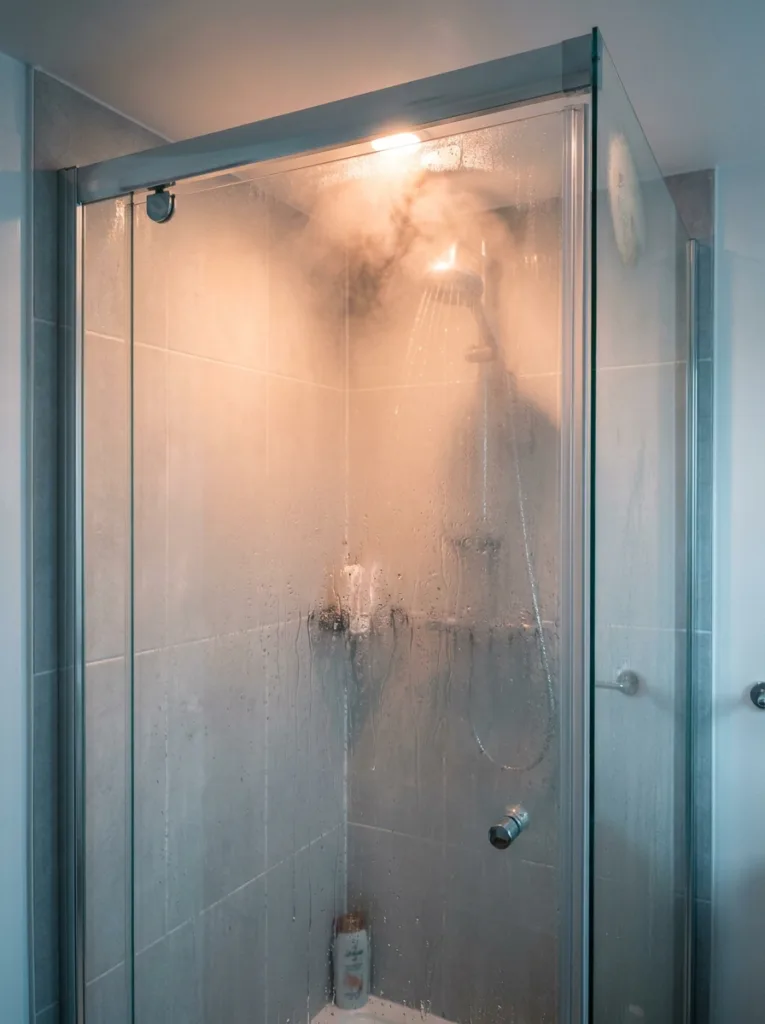 Steam rising from a hot shower running behind a glass door showing a common winter skincare mistake that damages dry skin