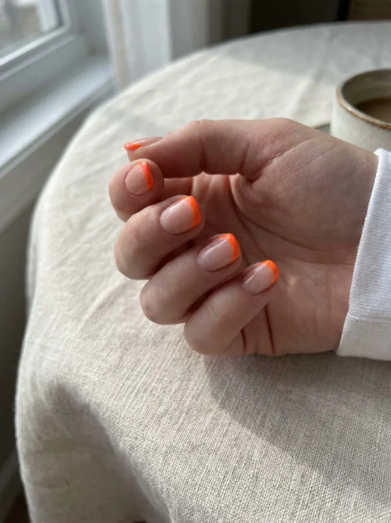 Neon French tip nail design in electric orange on fair skin