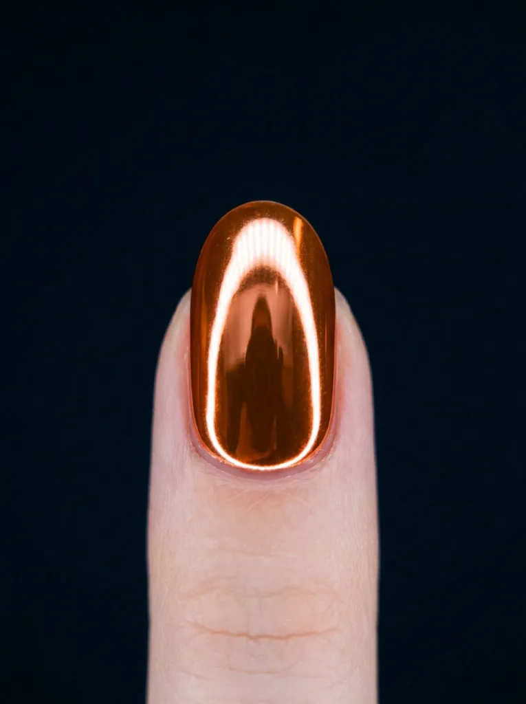 Close-up of mirror-finish orange chrome nail polish under studio light